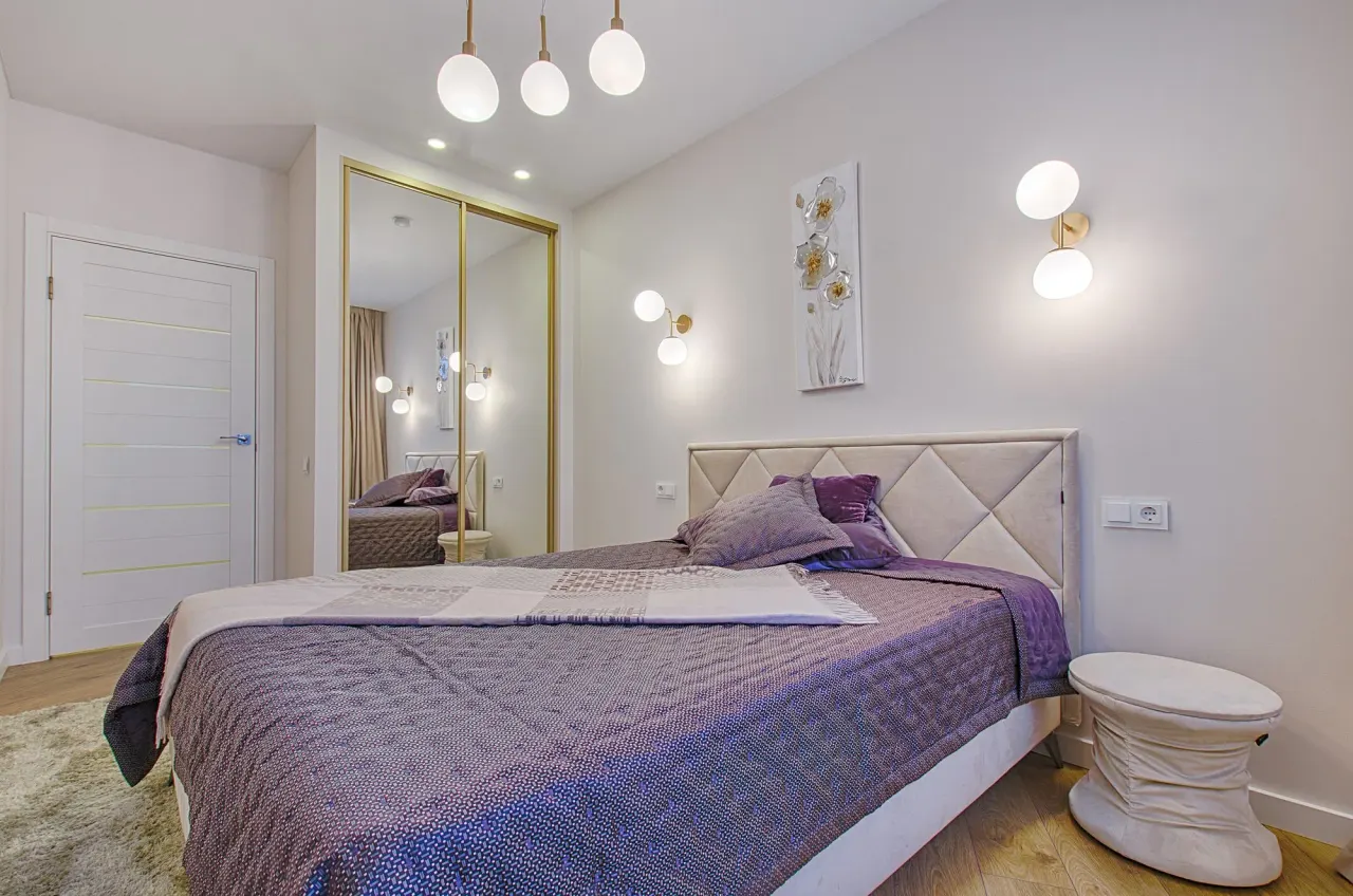 Dormitorio con cabecero tapizado, apliques de pared y armario de puertas correderas con espejo