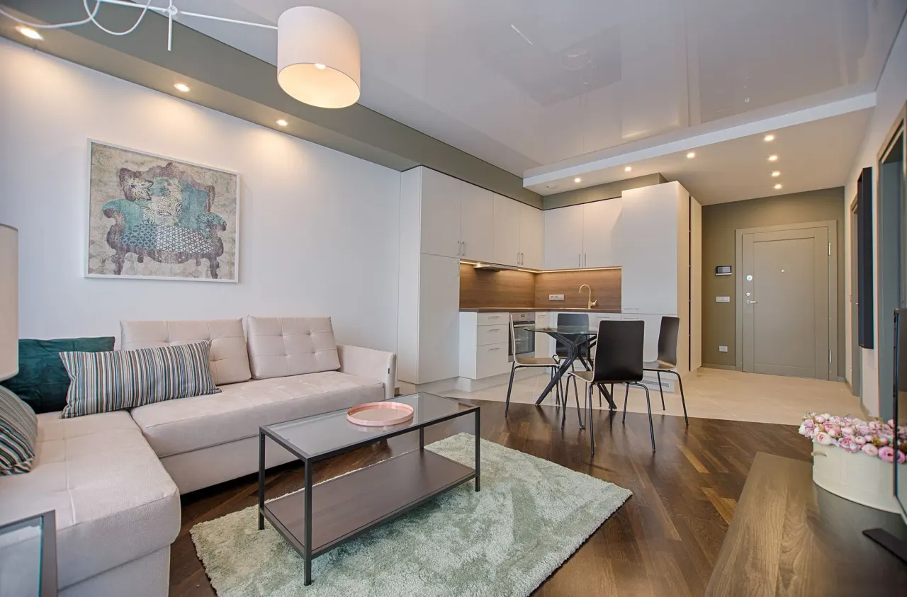 Salón con cocina abierta, sofá claro y suelo de madera oscura