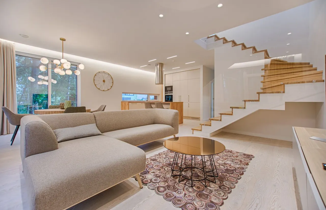 Salón diáfano con sofá en L y escalera de madera con barandilla de cristal