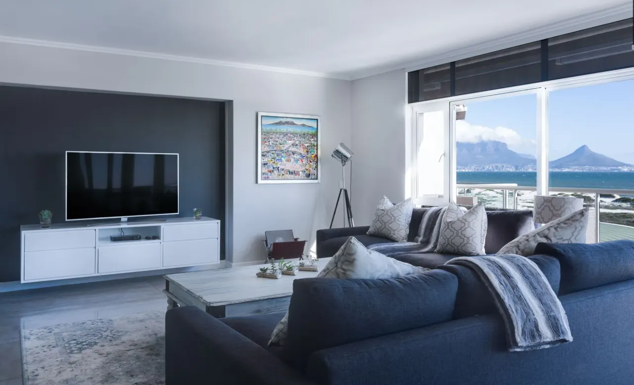 Salón con sofás azules, mueble de televisión blanco y ventanal con vistas al mar